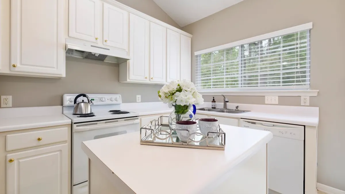 A tidy white kitchen with a clear island and a vase of white flowers